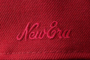 Close-up stacked view of four baseball caps in different colors: red with pink 'New Era' embroidery, turquoise with a black 'FEAR OF GOD' patch, black with a white, red, and blue MLB logo patch, and purple with a button visible.